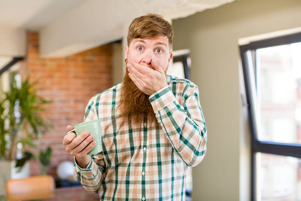 red hair man red hair man covering mouth with a hand and shocked or surprised expression with a coffee mug - Fotoğraf, Görsel