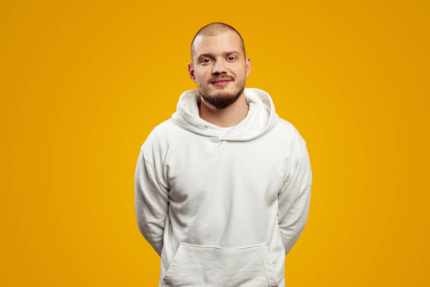 Serious adult bearded hipster man looking at camera, isolated over yellow background, wearing white hoodie. - Fotó, kép