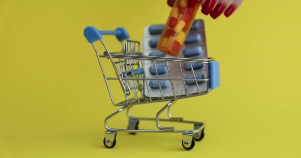 Kadın eli, ilaç şişesini sarı arka planda oyuncak alışveriş arabasına koyuyor. Markette ilaçlarla alışveriş kavramı. Sağlık ve organ için etkili ilaç - Video, Çekim