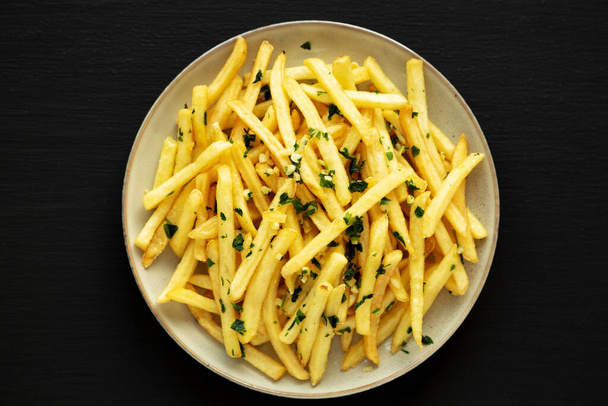 Garlic French Fries with Parsley on a Plate on a black background, top view. Overhead, from above, flat lay. - Photo, Image