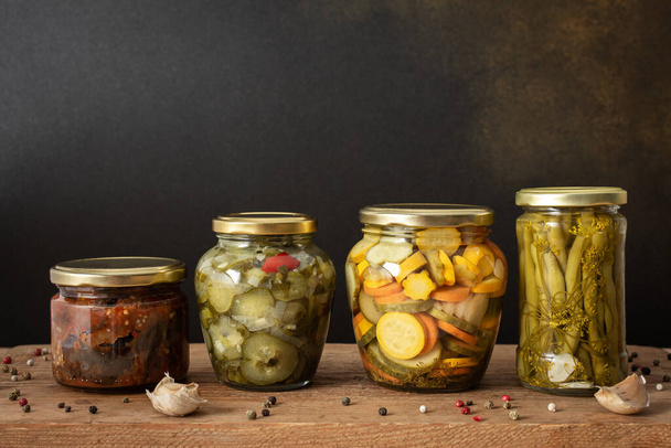 Preserving vegetables for the winter, canned vegetables in jars on a wooden table against a brown wall, pickled or fermented vegetables, copy space - Foto, imagen