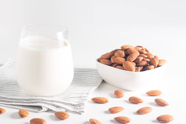 Organic almond milk in glass with raw almonds on white table  - Zdjęcie, obraz