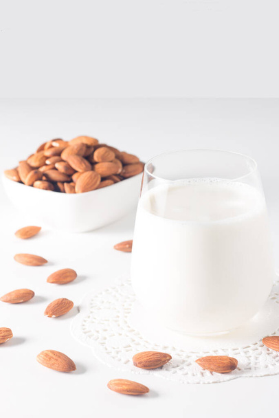 Organic almond milk in glass with raw almonds on white table  - Foto, Imagen