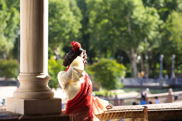 スペインのセビリアの広場でフラメンコジプシーの格好をした若い黒人女性。彼女はフリルと花の赤いショールでベージュのドレスを着ています。人類のフラメンコ文化遺産。舞踊の概念 - 写真・画像