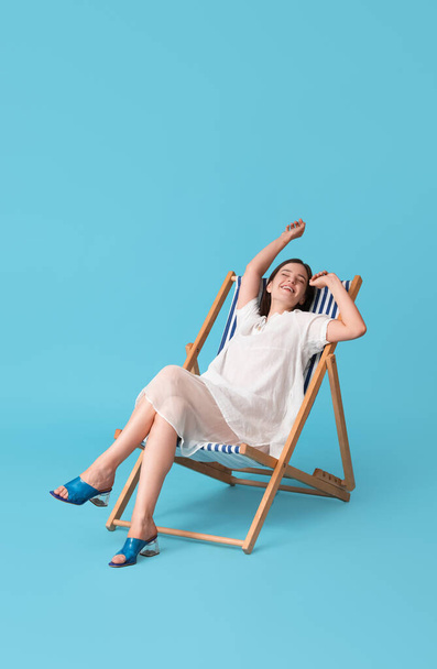 Mavi arka planda güverte sandalyesinde dinlenen genç bir kadın. - Fotoğraf, Görsel