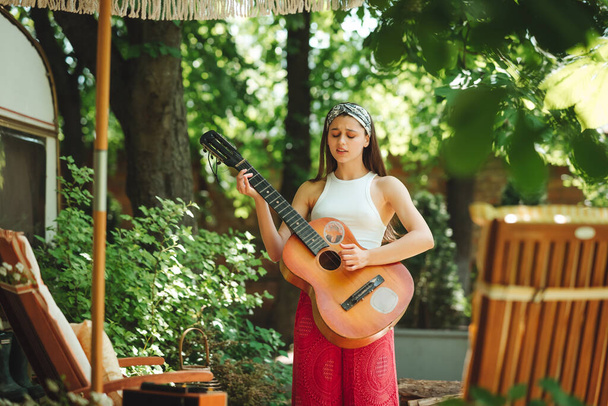 ハッピーヒッピーの女の子は、キャンパートレーラーでギターを弾くのに楽しい時間を過ごしています。休日、休暇、旅行のコンセプト。高品質の写真 - 写真・画像