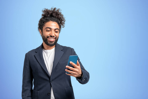 Middle eastern businessman happy looking at phone, video call and connection on empty blue background. Concept of social media. Copy space - Zdjęcie, obraz