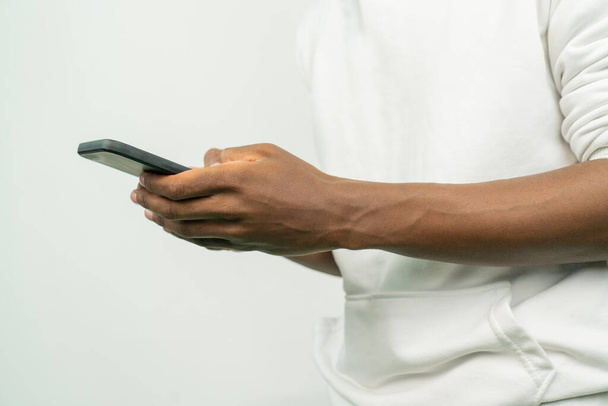 φωτογραφία ενός Αφροαμερικανού που χρησιμοποιεί κινητό ενώ στέκεται σε λευκό φόντο. - Φωτογραφία, εικόνα