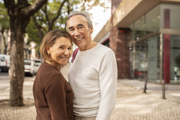 Mosolygó idősebb pár alkalmi ruha nézi Camera álló utcában a szabadban. Boldog érett házastársak férfi és nő együtt pózolnak a városi területen. Szabad hely a szövegnek - Fotó, kép