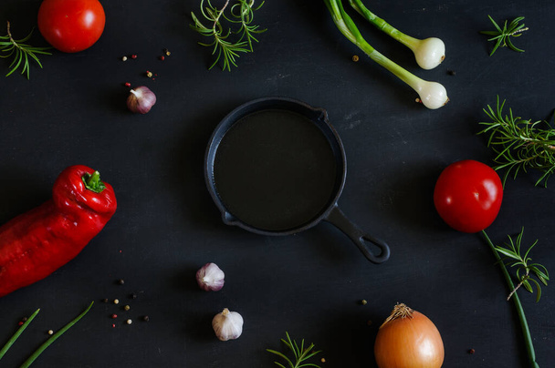 Empty cast iron skillet and vegetables on a black shabby background. View from above. Selective focus in natural light - 写真・画像