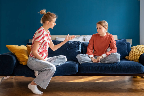 Mom scolds introvert teenage girl with heavy admonition. Problems in communication with children of adolescence transitional age. Irritated mother sit on couch talk to bored ignoring teenager at home  - Photo, Image