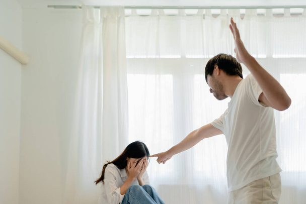 Домашнее насилие, азиатский муж угрожает жене, напуганная мать обнимает ее, когда она сидит вместе на кровати - Фото, изображение
