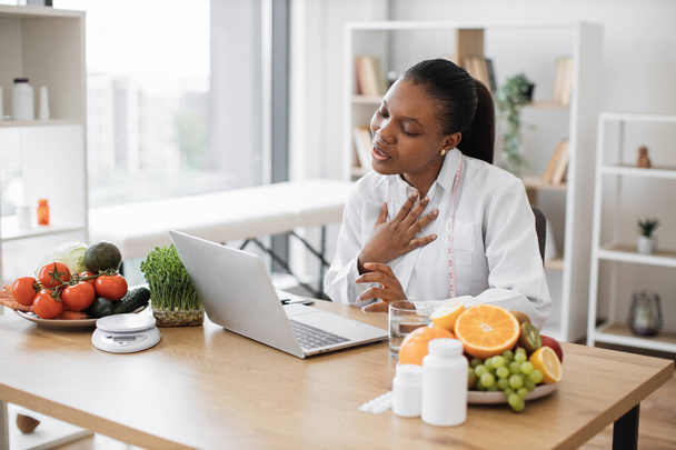 Friendly multiethnic female making video call via wireless device at doctors workplace in hospital. Attentive dietitian providing online consultation about clients progress in identifying foods. - Foto, imagen