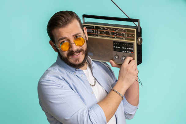 Young lebanese man using retro tape record player to listen music, disco dancing of favorite track, having fun, entertaining, fan of vintage technologies. Arabian guy isolated on blue background - Fotografie, Obrázek