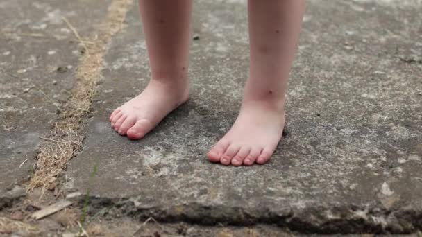 Egy kislány áll mezítláb a betonon. Nyáron szandál, forró nyár és pihenés. - Felvétel, videó