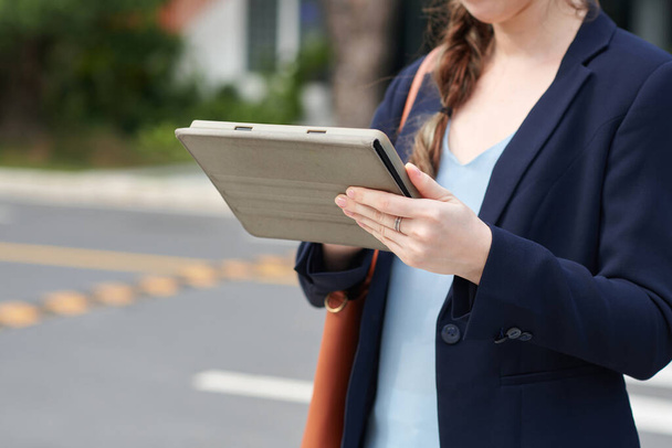 Cropped image of businesswoman standing outdoors and reading report on tablet computer - Foto, imagen