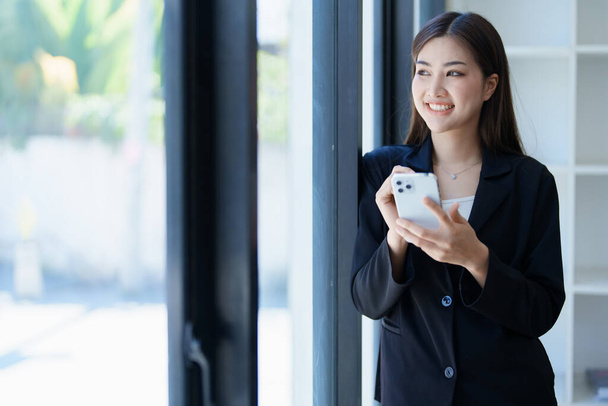 オフィスのアジアのビジネス女性は、スマートフォンや作業中に幸せと陽気です。女性従業員は成功とボーナスの興奮を表現する - 写真・画像