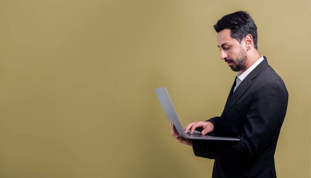 Successful businessman in black suit with innovative tech concept, standing pose and holding laptop and smiling with excitement on copyspace background for promotion or advertisement. Fervent - 写真・画像