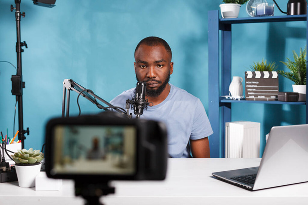 Blogger afroamericano grabando video con cámara profesional en su estudio en casa. Vlogger hablando en micrófono mientras transmite en vivo y crea contenido digital para el canal de Internet - Foto, imagen