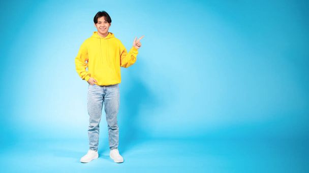 Check this. Happy young asian guy pointing up at free space for text, expressing positive emotion and demonstrating empty place for advertisement standing on blue background, full length, panorama - Fotó, kép