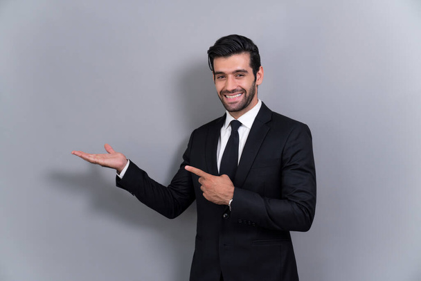 Αυτοπεποίθηση επιχειρηματίας με επίσημο κοστούμι δείχνοντας δάχτυλο και χέρι κρατώντας χειρονομία για να δείξει την προώθηση ή τη διαφήμιση σε κενό χώρο με ενθουσιασμένοι έκφραση του προσώπου σε απομονωμένο φόντο. Έντονη - Φωτογραφία, εικόνα