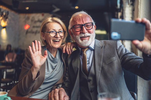 Starší pár starší muž a žena kavkazský manžel a manželka přičemž selfie fotky self portréty nebo video hovor, zatímco sedí v kavárně nebo restauraci bufetu - Fotografie, Obrázek