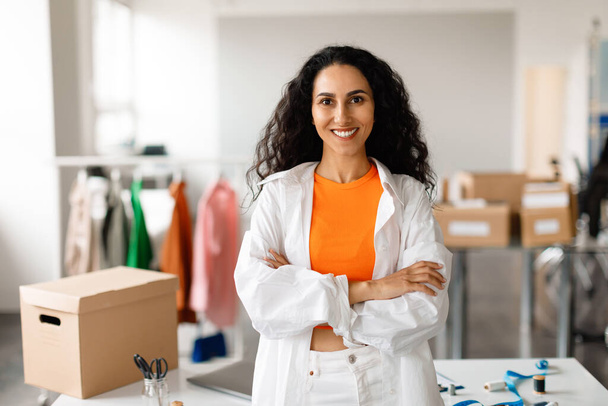 Professional Clothing Designer Woman Standing With Folded Hands At Modern Fashion Design Studio Interior, Smiling To Camera. Small Business, Boutique Ownership And Entrepreneurship - Фото, зображення