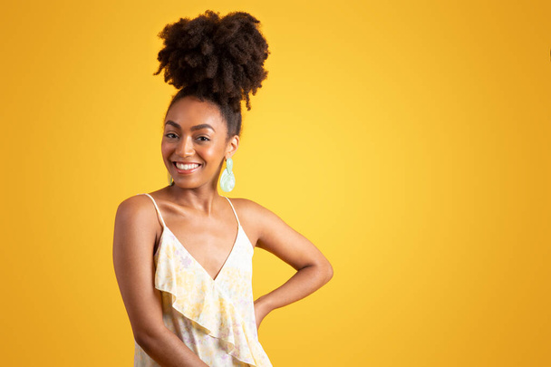 Fröhlich selbstbewusste junge schwarze Frau im Kleid blickt in die Kamera, genießt Urlaub, Wochenende und Freizeit, isoliert auf gelbem Hintergrund, Atelier. Lifestyle, Modeverkauf, Werbung und Angebot - Foto, Bild