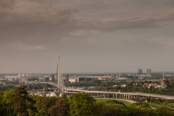 Panorama y horizonte de las altas subidas del distrito de Novi Beograd con el puente Ada Most con calles de carretera en frente al atardecer. Nuevo Belgrado es el distrito financiero de la ciudad. - Foto, Imagen