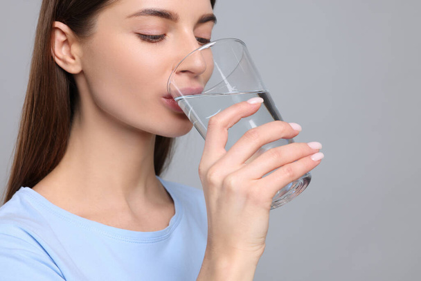 Healthy habit. Woman drinking fresh water from glass on grey background - Photo, image