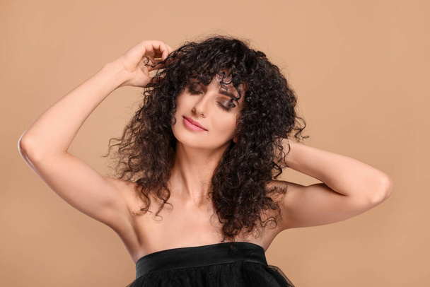 Beautiful young woman with long curly hair on beige background - Fotografie, Obrázek