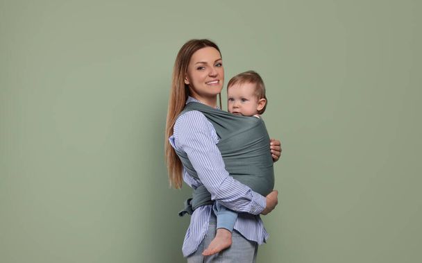 Madre sosteniendo a su hijo en una envoltura de bebé sobre fondo de oliva - Foto, imagen