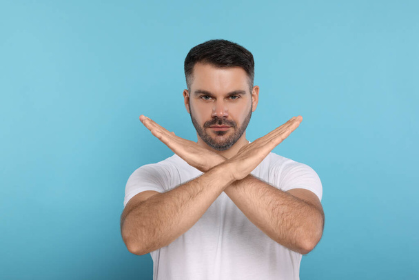 Handsome man with crossed hands on light blue background. Stop gesture - Foto, immagini