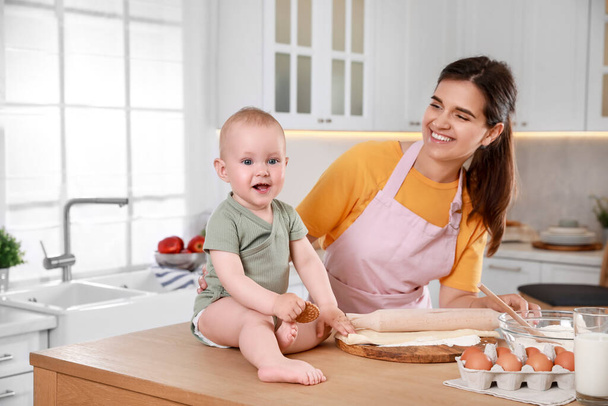 Glückliche junge Frau und ihr süßes kleines Baby kochen zusammen in der Küche - Foto, Bild