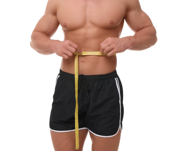 Athletic man measuring waist with tape on white background, closeup. Weight loss concept - Photo, image