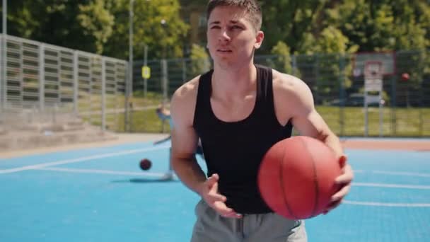 Атлетичный белый мужчина в спортивной одежде играет в баскетбол, успешно бросает мяч в корзину ринга. Молодой парень на городской летней площадке. Тренировка на спортивной площадке. Мотивация. На открытом воздухе - Кадры, видео