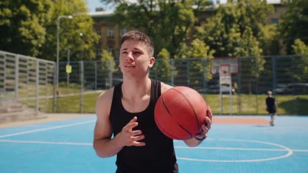Homme caucasien athlétique en vêtements de sport jouant au basket-ball, lance avec succès la balle dans l'anneau de panier. Jeune homme au tribunal d'été de la ville urbaine. routine de remise en forme sur terrain de sport. Motivation. À l'extérieur - Séquence, vidéo