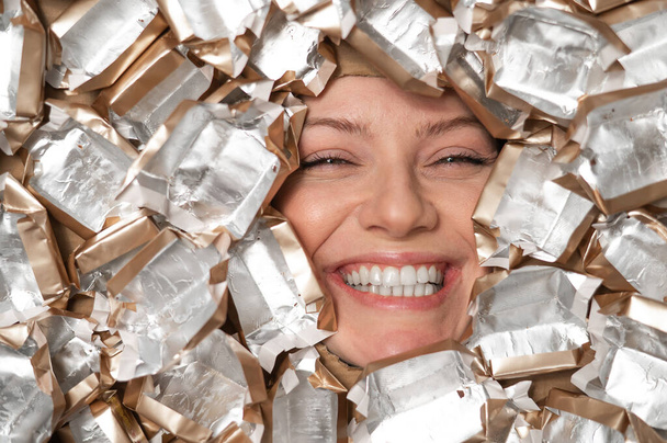 The face of a Caucasian woman surrounded by candy wrappers - Photo, Image