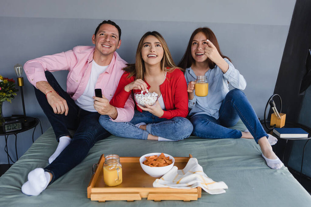 Grupo de amigos latinos sentados en la cama viendo televisión o película en casa en México América Latina, gente hispana divirtiéndose - Foto, Imagen