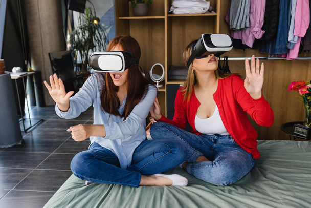 Латинська пара жінок, які грають у відеоігри віртуальної реальності на ліжку в їхньому будинку разом у Мексиці Латинській Америці, його друзі - Фото, зображення