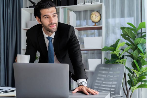 Сучасний професійний бізнесмен на сучасному офісному столі використовує ноутбук для роботи з кавою в руці. Рішучий офісний працівник, який працює на комп'ютерному ноутбуці у своєму офісному робочому просторі. палкий
 - Фото, зображення