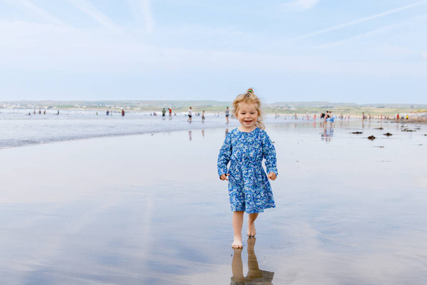 Egy aranyos kislány a Ballybunion szörfös strandon, aki jól érzi magát Írország nyugati partjainál. Boldog gyermek élvezi az ír nyár és napos nap a családdal - Fotó, kép