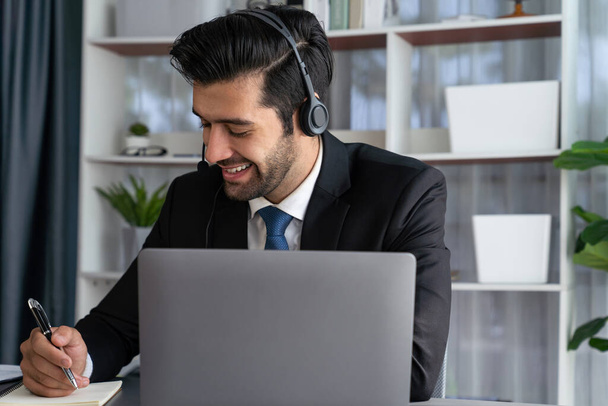 Male call center operator or telesales representative siting at his office desk wearing headset and engaged in conversation with client providing customer service support or making a sale. fervent - Valokuva, kuva