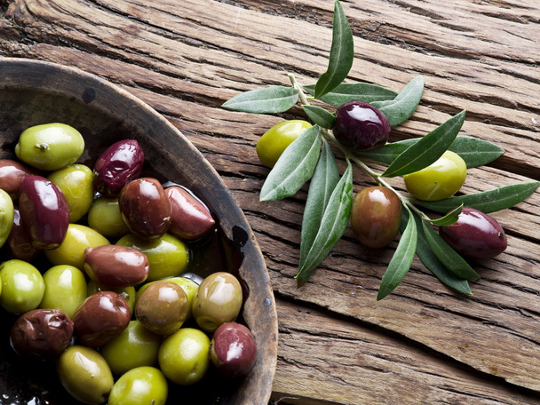 Wooden bowl full of olives and olive twigs besides it. - Foto, afbeelding