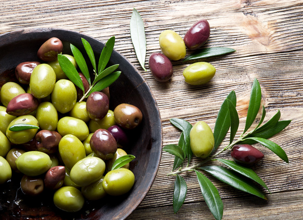 Wooden bowl full of olives and olive twigs besides it. - Photo, Image