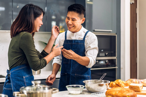 Jeune couple de famille asiatique ayant plaisir à cuisiner avec de la pâte pour biscuit maison et ingrédient gâteau sur la table.Couple heureux qui cherchent à préparer la nourriture la pâte dans la cuisine - Photo, image