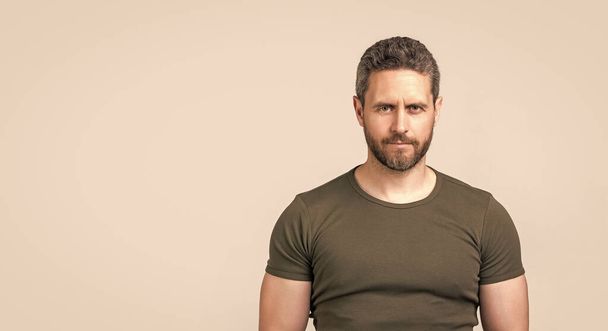 caucasian guy with stubble in studio with copy space. photo of caucasian guy with stubble. caucasian guy with stubble wear tshirt. caucasian guy with stubble isolated on grey background. - Photo, image