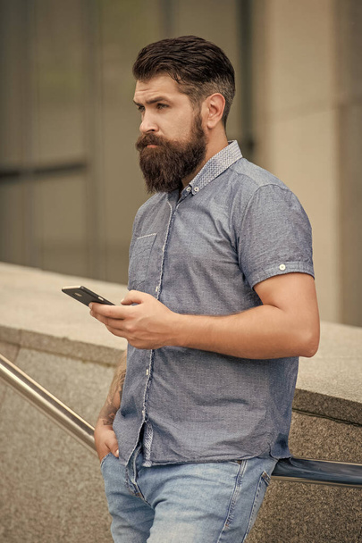 Bearded guy using mobile phone outdoors. Serious guy using device for mobile sms messaging, mobile communication. Mobile technology. - 写真・画像