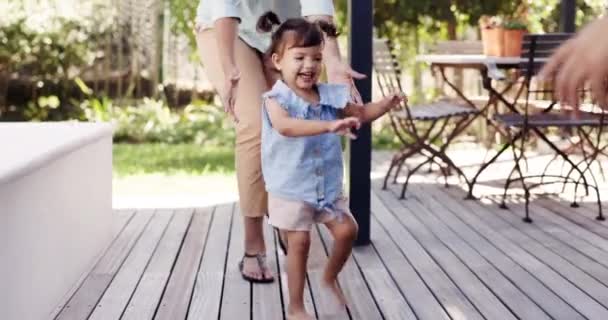 Happy, girl or child learning to walk or dance with parents in outdoor garden, backyard or toddler on the deck of home with family. Mom, dad and excited kid walking, running or dancing with happiness. - Filmagem, Vídeo