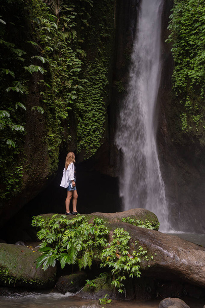 A woman standing in front of waterfall in the jungle. Travel Indonesia. Hidden beauty of the island - Valokuva, kuva